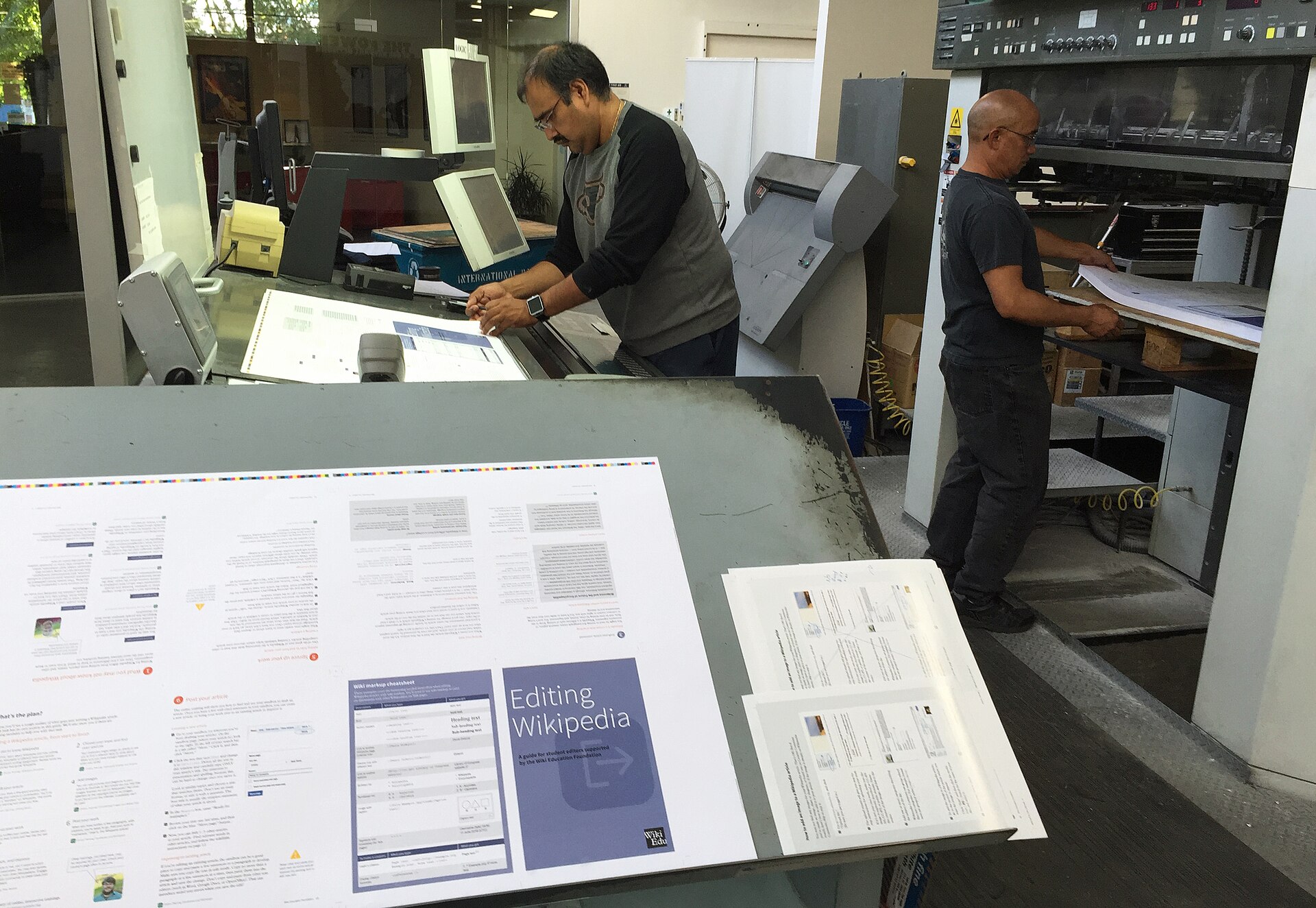 Press operators checking a printed sheet against the proof
